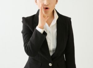 口元に手を当てて話しかけようとするスーツ姿の女性